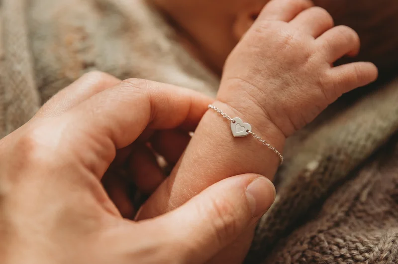 Mother holding newborn baby's wrist next to a delicate silver baby bracelet — size comparison for newborn baby bracelet UK