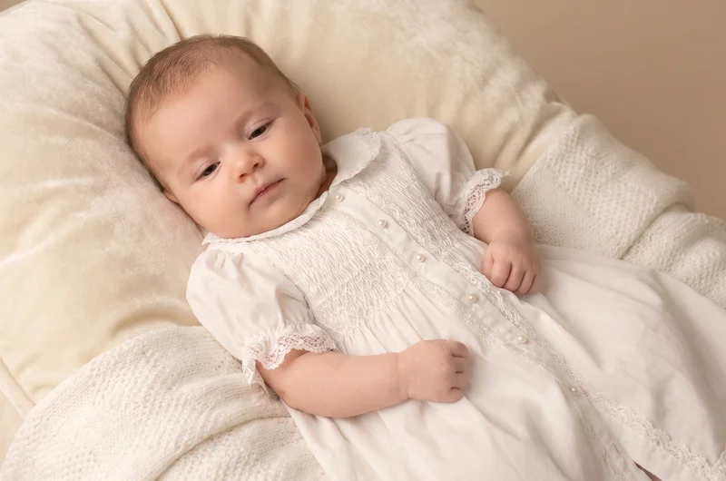 Baby girl in white christening dress UK 2026 — lace and smocked styles