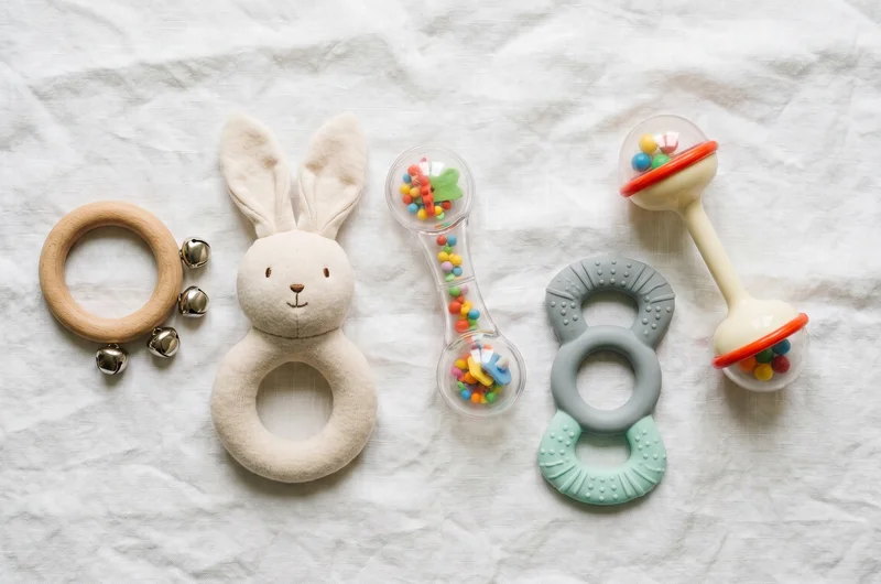 Baby rattle UK 2026 — flat lay of five different types including wooden, soft, sensory and wrist rattles on white linen