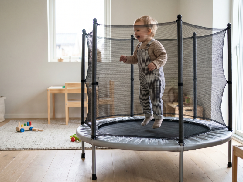 Toddler bouncing on mini indoor trampoline with safety net enclosure in family home