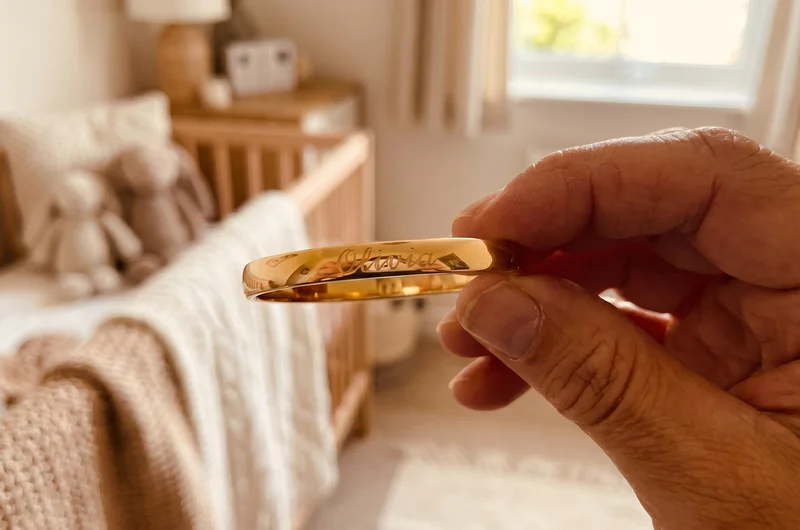 Personalised engraved baby gold bangle with baby's name — held between parent's fingers
