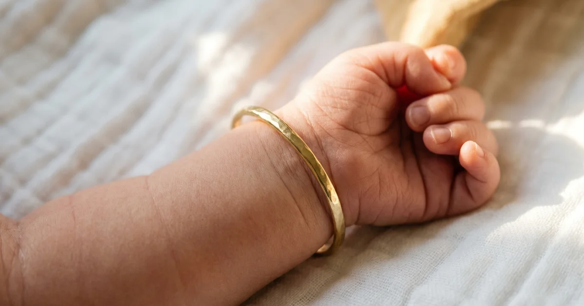 Baby's gold bangle UK 2026 — delicate 9ct gold bangle on a newborn's wrist